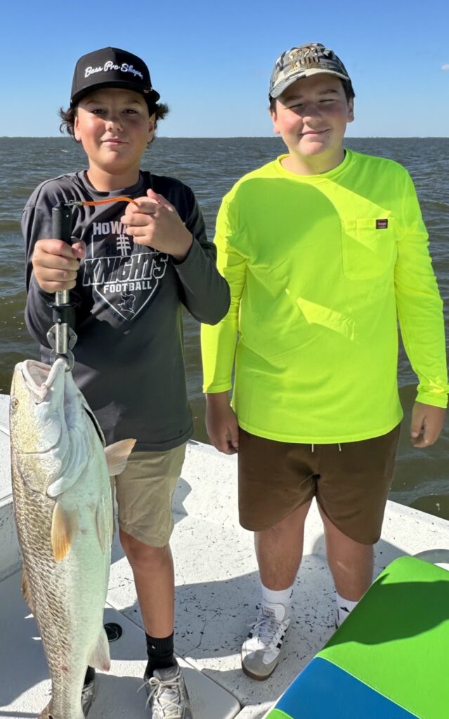 Two young fishermen, one holding a large redfish